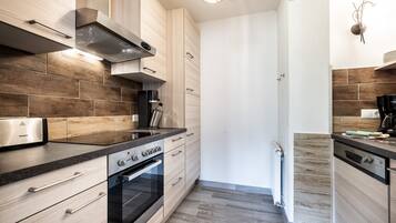 A modern kitchen with wooden cabinets, a stainless steel range hood, a built-in oven, and a coffee machine.