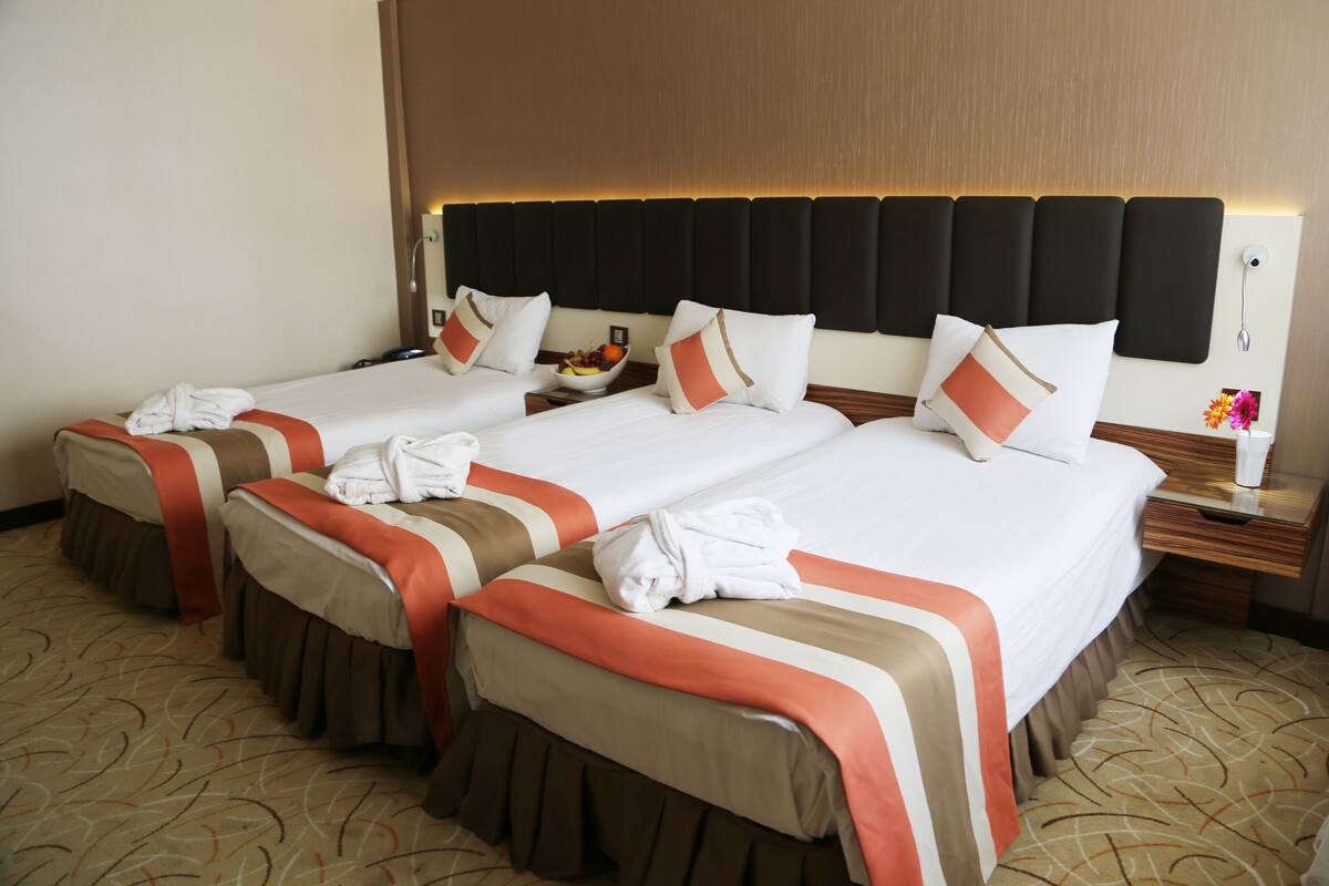 A hotel room with four beds, each with a headboard, a bedside table, and a nightstand.
