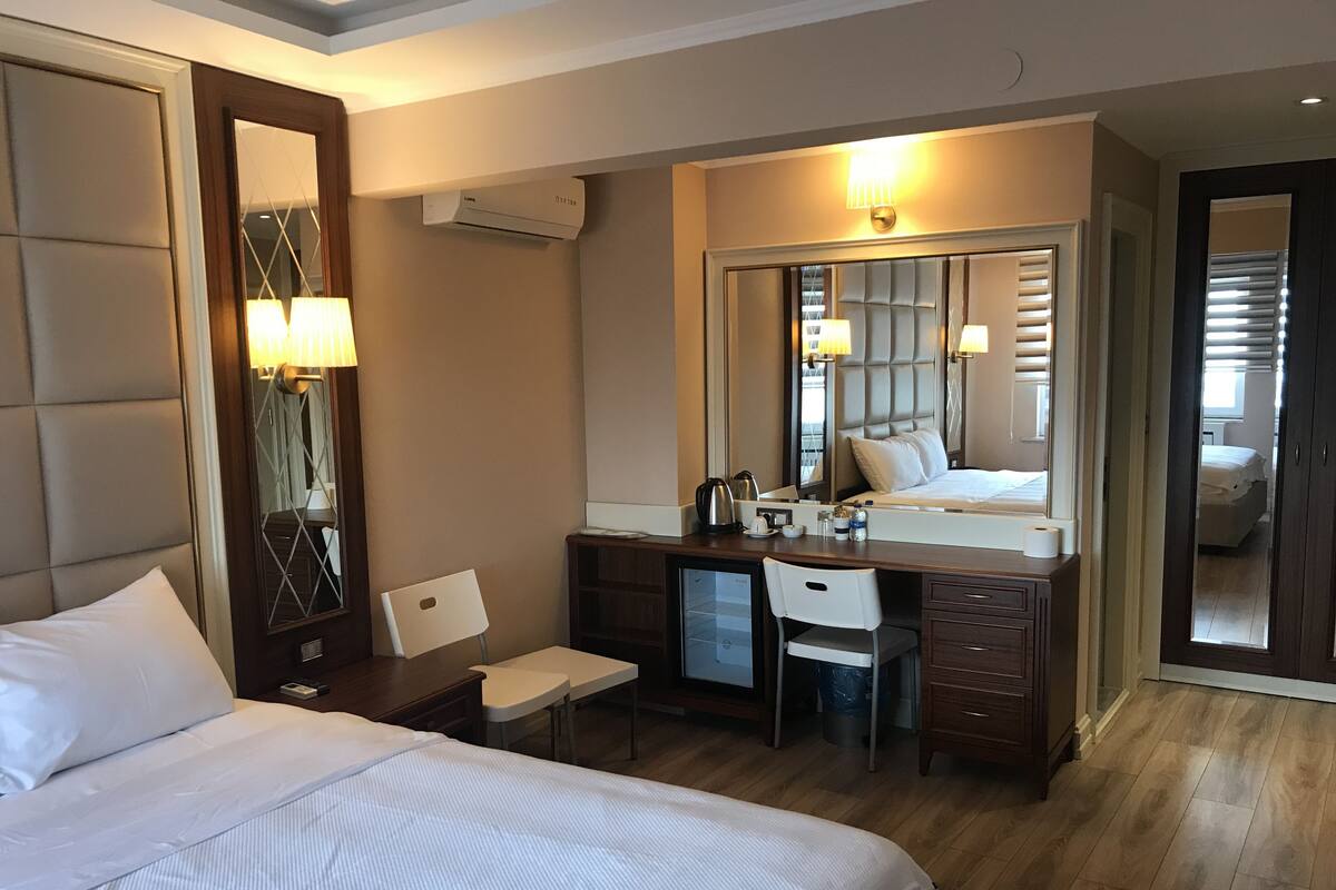 A hotel room with a large bed, a desk with a chair, a mirror, and a dresser.