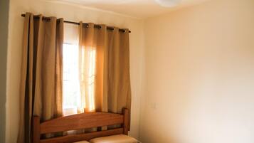Un dormitorio con cama de madera, cortinas color beige y ventilador de techo.