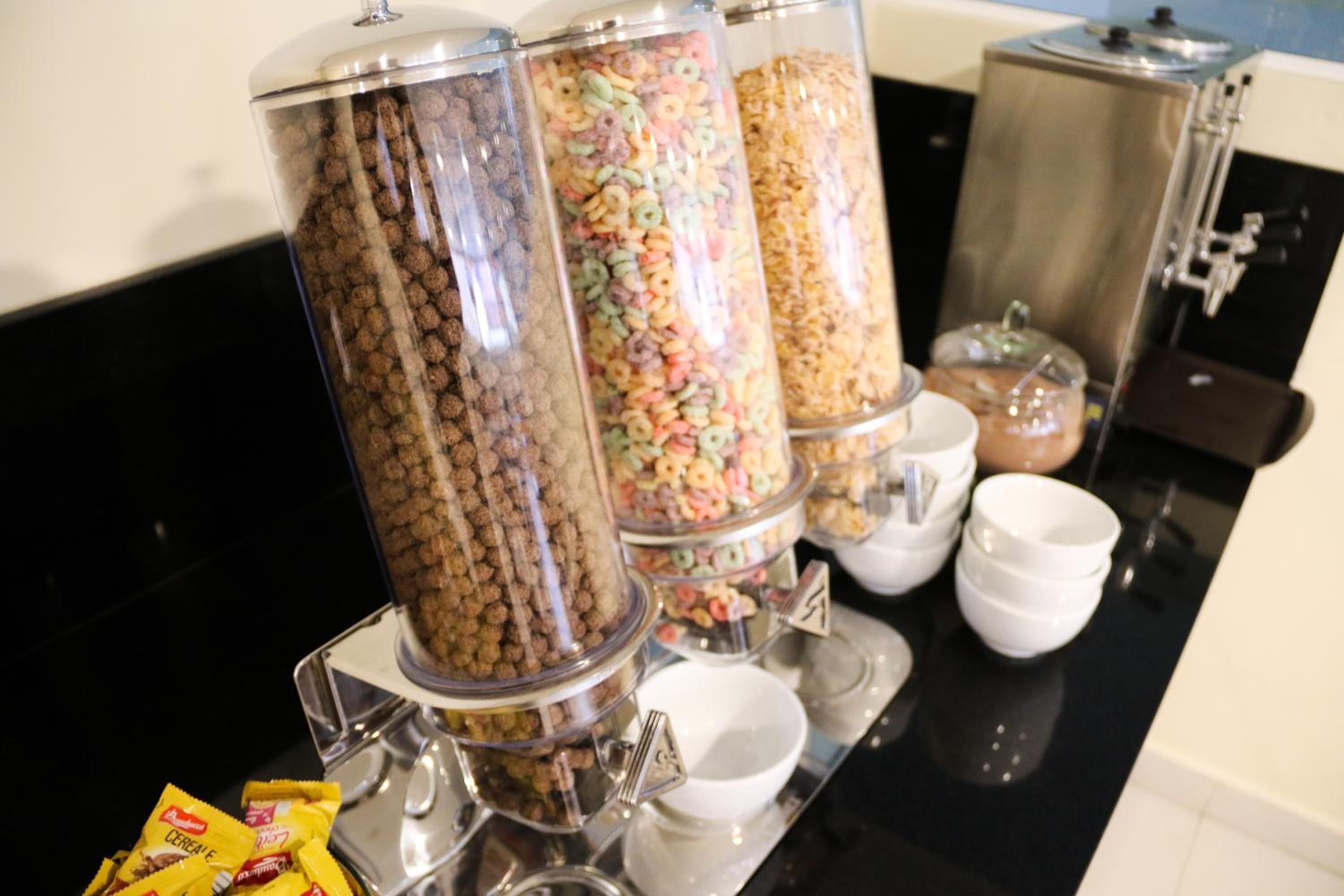 Ein Buffet mit verschiedenen Speisebehältern, darunter Frühstückscerealien und Müsliriegel, auf einer schwarzen Arbeitsplatte.