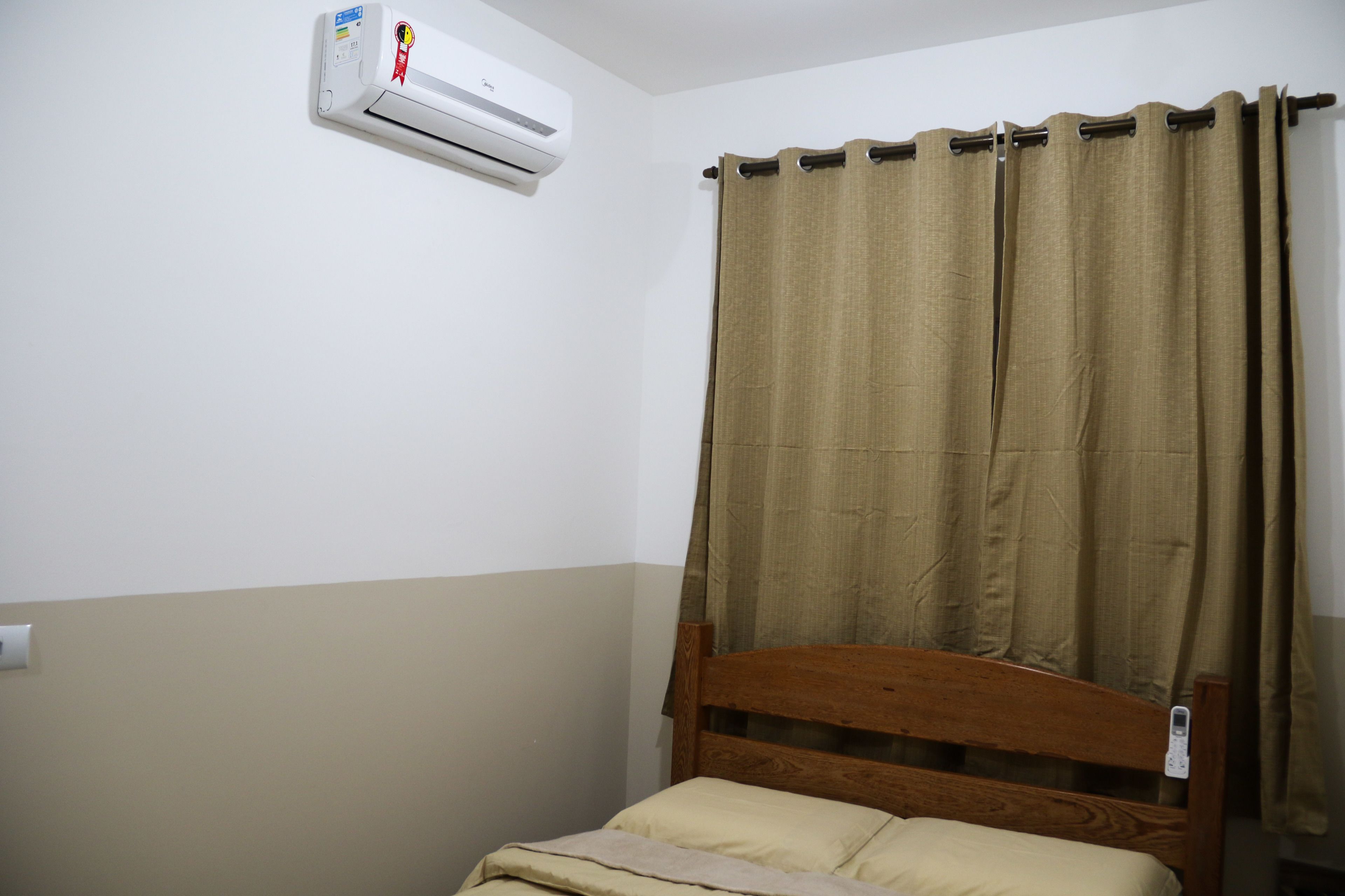 A single bed with a wooden headboard, beige bedding, and a brown curtain.