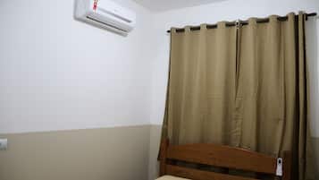 A single bed with a wooden headboard, beige bedding, and a brown curtain.