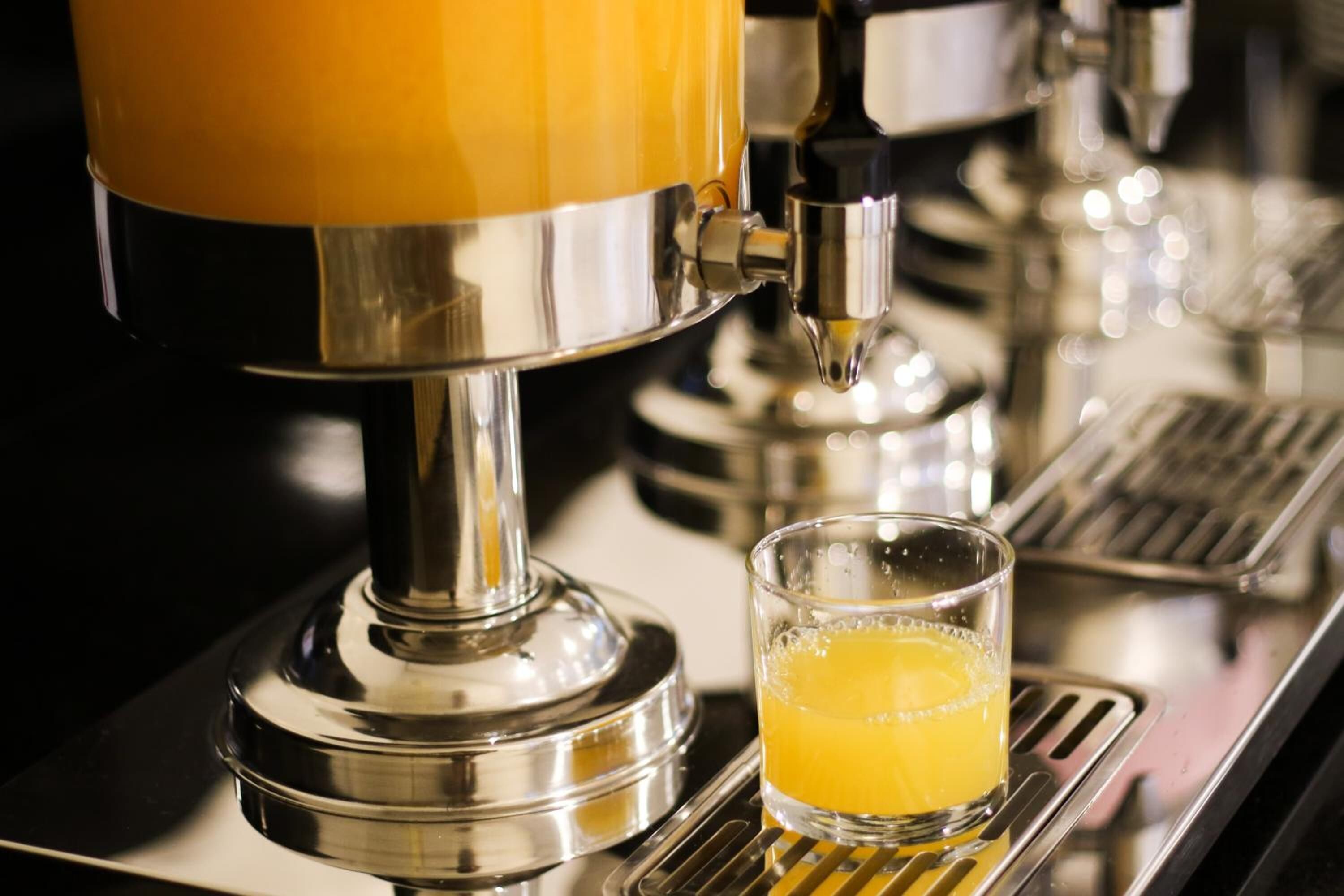 A coffee machine dispensing orange juice into a glass.