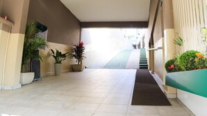 Un vestíbulo de hotel con piso de baldosas, plantas en macetas, una escalera y una alfombra verde que conduce a la escalera.