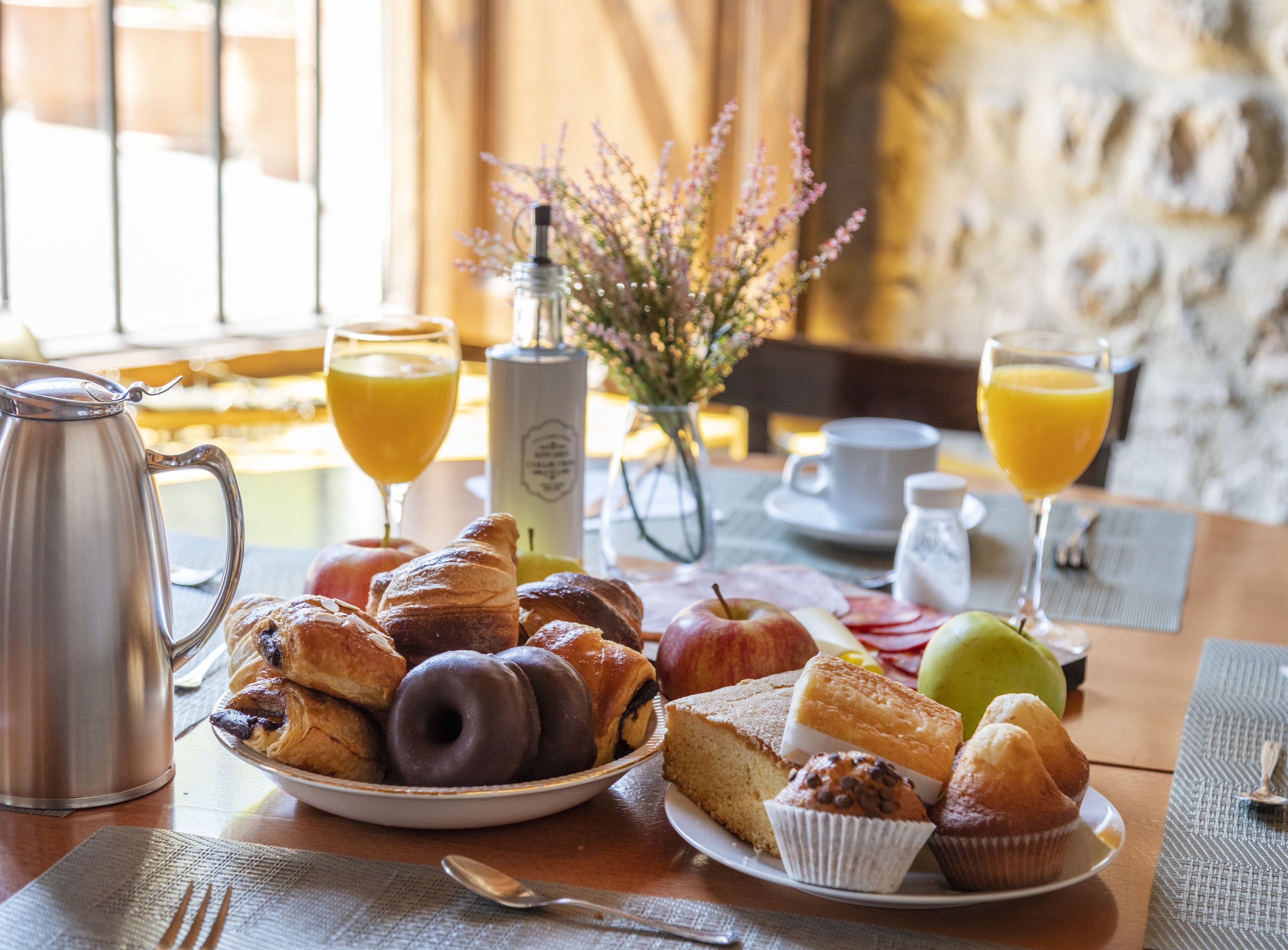 Una mesa de desayuno con pasteles, una cafetera y vasos de jugo de naranja.