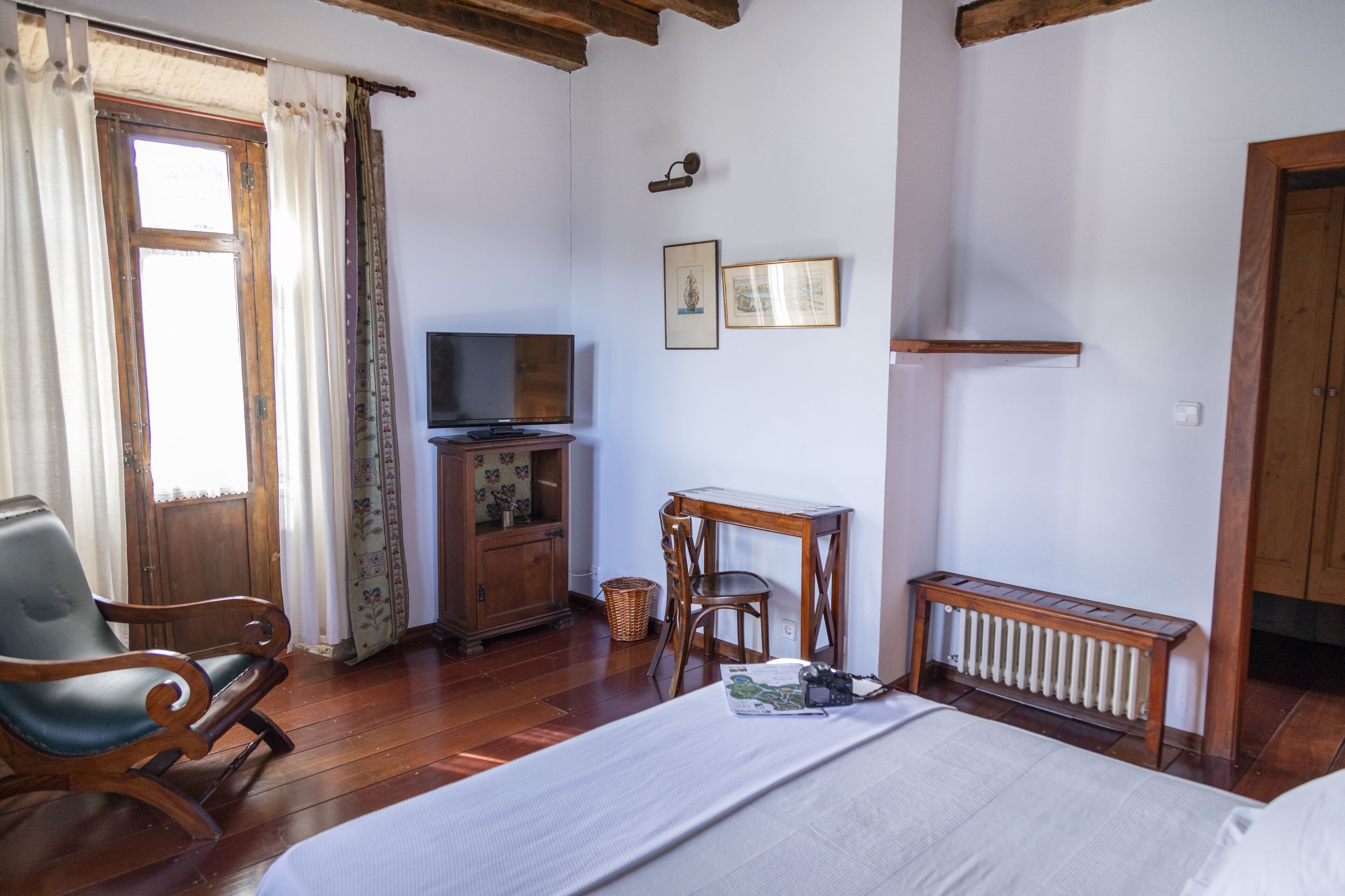 A bedroom with a bed, a wooden desk, a chair, a television, and a radiator.