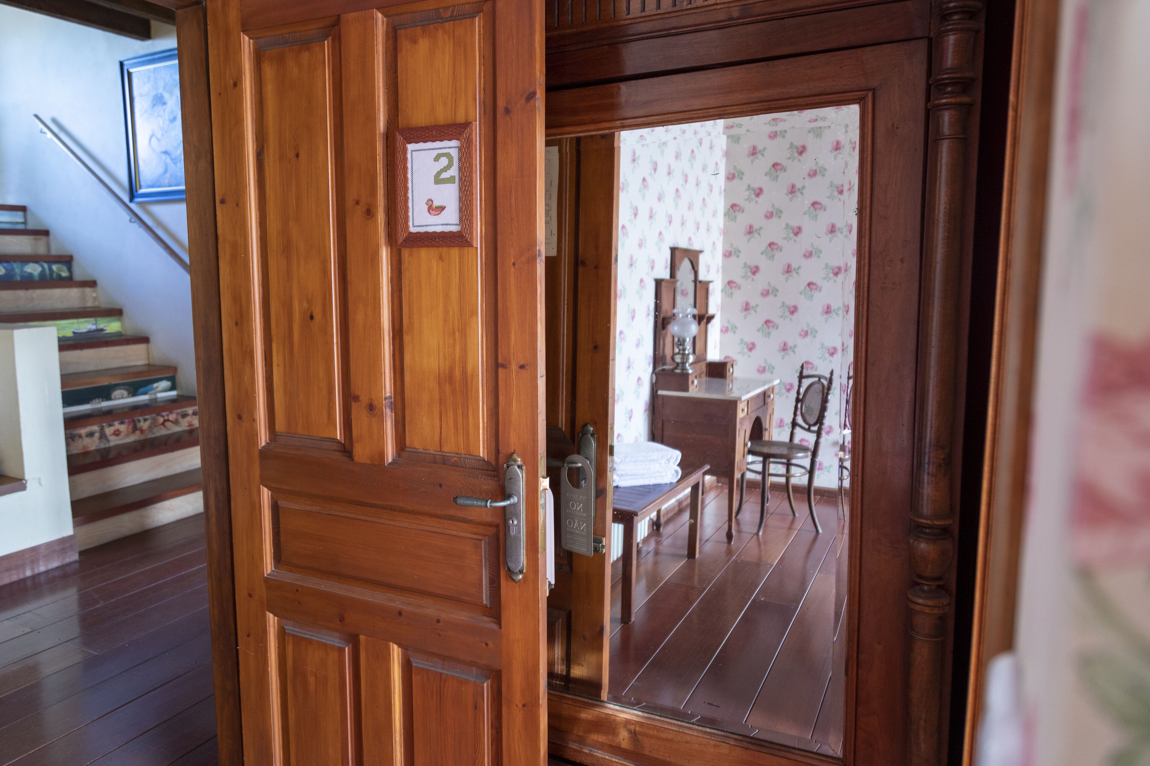 Una porta in legno con una targa con il numero '2', una scala e una sala da pranzo con carta da parati floreale.