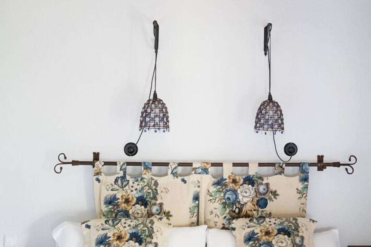 Un dormitorio con techo de madera, una cama con ropa de cama floral y dos lámparas fijadas a la pared.