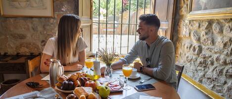 Un desayuno con una pared de piedra, una ventana con vistas a la vegetación y una mesa con comida y bebidas.