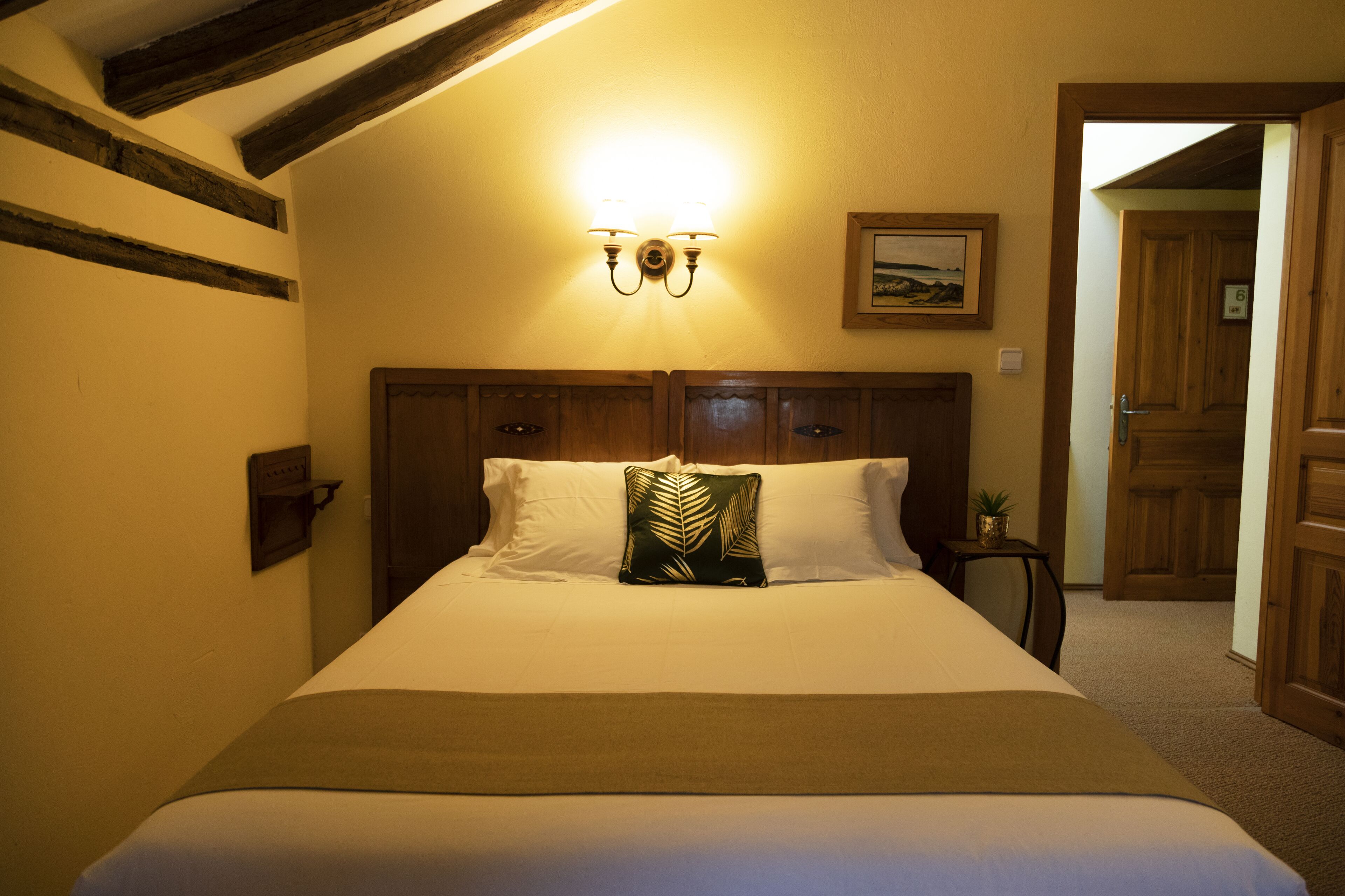Una habitación de hotel con una cama grande, cabecera de madera y una lámpara fijada a la pared.