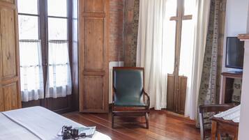 Een kamer met houten vloeren, een bed met een wit laken, een groene stoel, een houten tafel met een televisie, en een raam in kruisvorm.