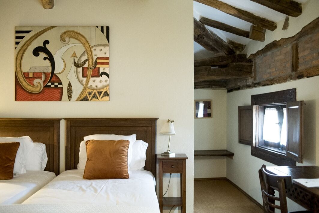 A bedroom with two beds, a wooden headboard, a bedside table with a lamp, and a large abstract painting on the wall.