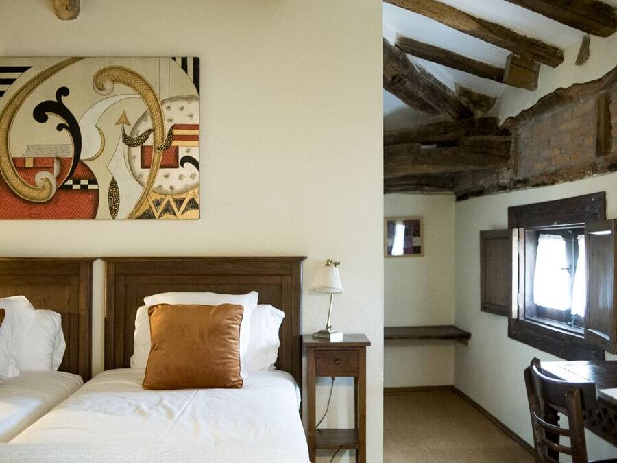 A bedroom with two beds, a wooden headboard, a bedside table with a lamp, and a large abstract painting on the wall.