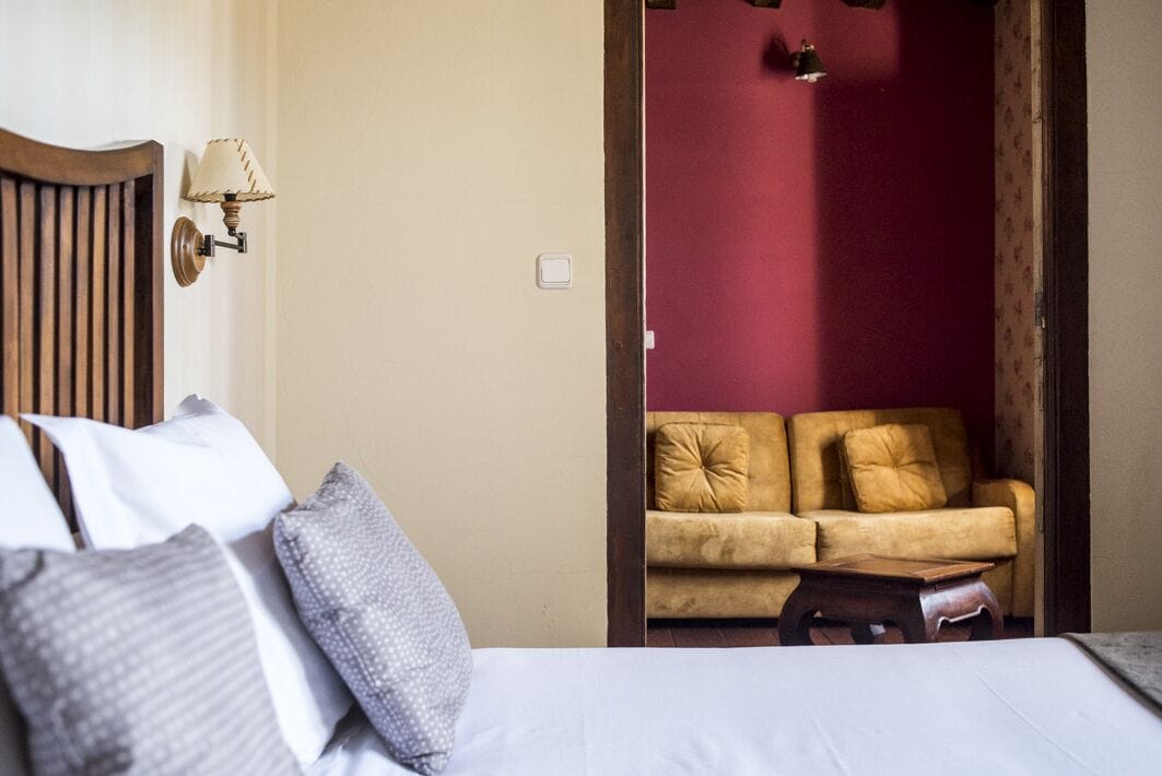 Een slaapkamer met een bed, kussens, een nachtkastje, een wandlamp en een rode muur.