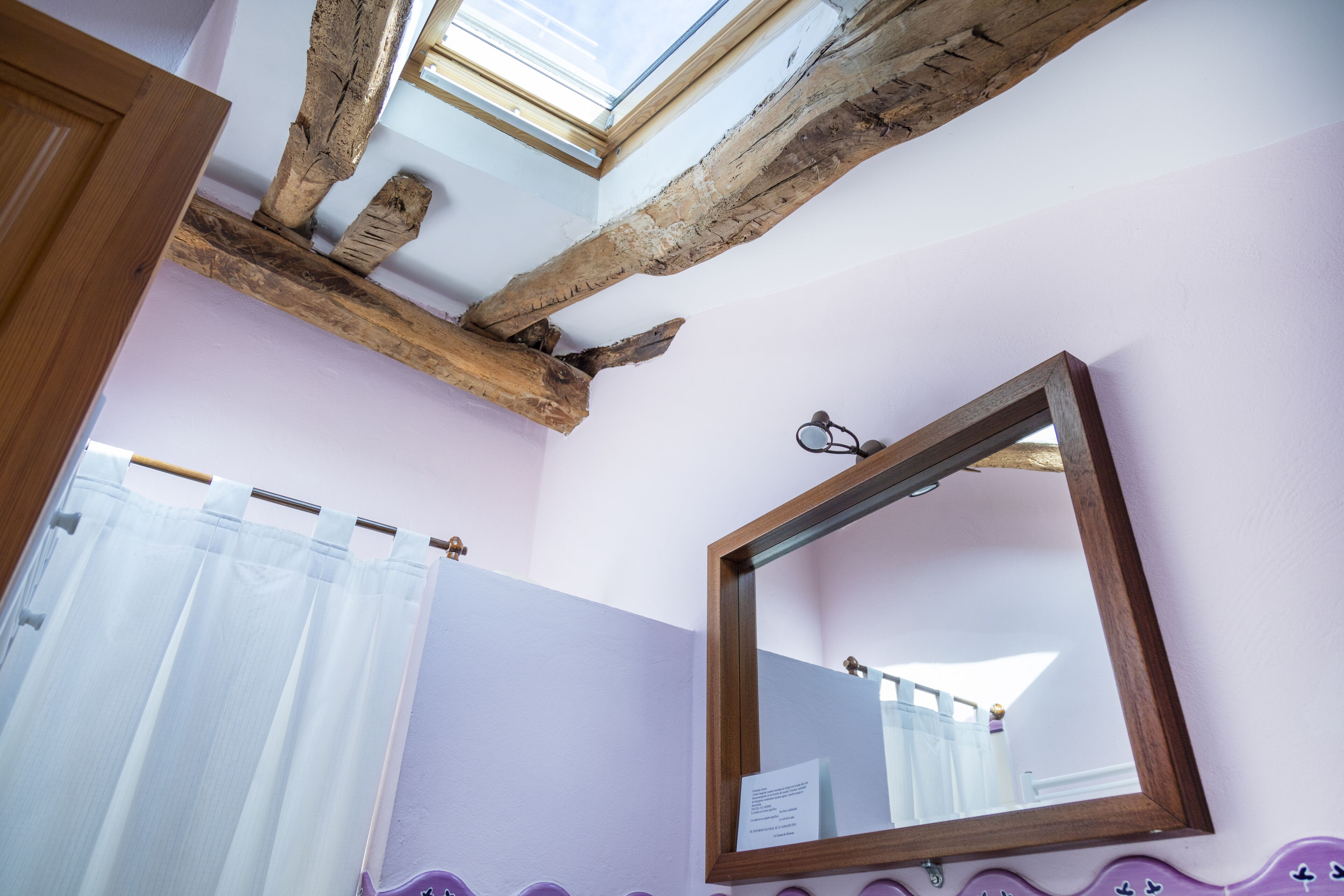 Un baño con tragaluz, vigas de madera, espejo y un borde decorativo morado.