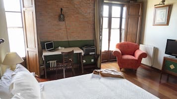 Una habitación con una cama, un escritorio con ordenador, un sillón rojo y una televisión.