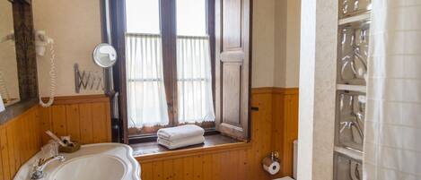 Un baño con tocador de madera, lavamanos, inodoro y ventana con cortinas.