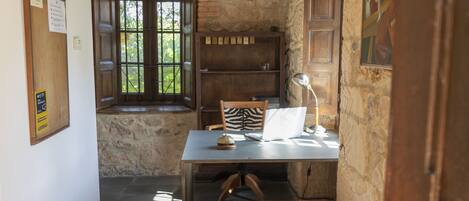 A rustic room with a wooden table, a bench, a window with a view of trees, a bookshelf, and a door with a painting.