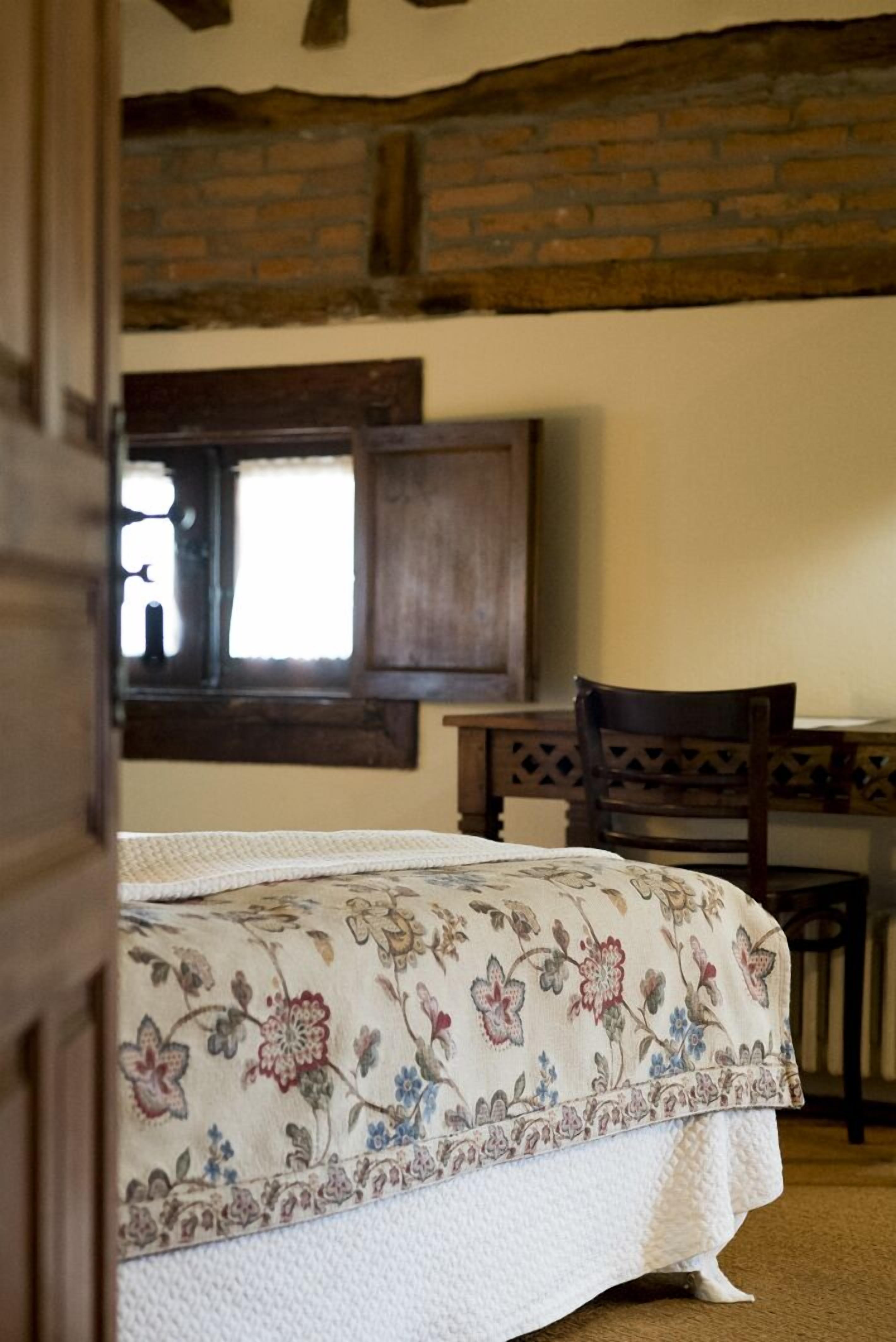 Een slaapkamer met een bed, een houten bureau en een raam.