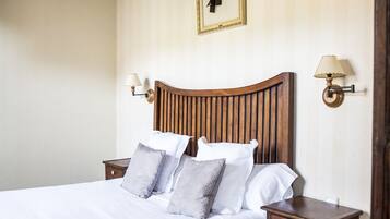 Een netjes opgemaakt bed met witte lakens en grijze kussens, een houten hoofdbord en twee nachtkastjes met lampen.