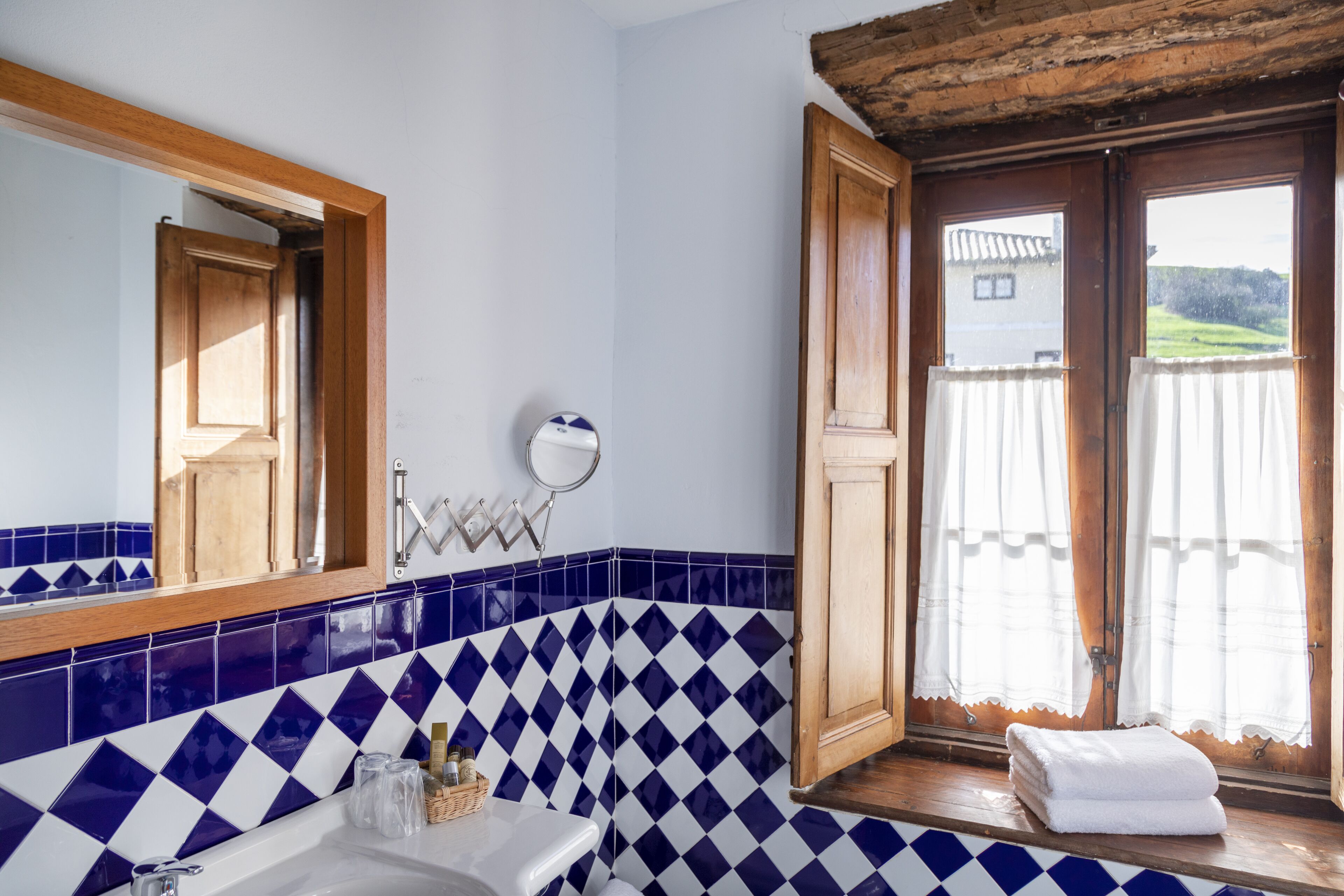 A bathroom with a blue and white checkered tile backsplash, a wooden door, and a view of a house through a window.