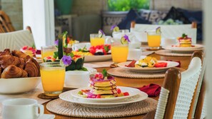 A breakfast setting with croissants, fruit, and orange juice on a table. - Villa Little Mannao by Villa Finder (Kerobokan)