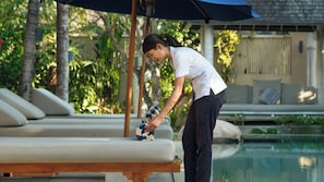 A person adjusting a towel on a lounge chair by a poolside. - Villa Little Mannao by Villa Finder (Kerobokan)