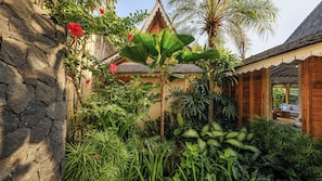 A tropical garden with a stone wall, various plants, and a wooden structure. - Villa Little Mannao by Villa Finder (Kerobokan)
