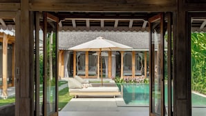 A glass-enclosed outdoor lounge area with a pool, a wooden pergola, and a view of a bedroom with a bed and curtains. - Villa Du Ho by Villa Finder (Kerobokan)