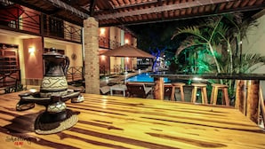 An outdoor dining area with a pool, wooden tables, and a decorative urn. - Hotel Pousada Sol & Lua (Paracuru)