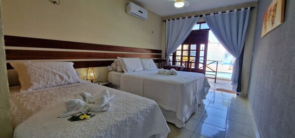 A hotel room with two beds, each with a white bedspread and pillows, a bedside table with a lamp, and a window with curtains. - Hotel Pousada Sol & Lua (Paracuru)