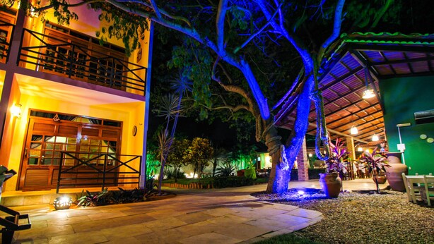 A well-lit outdoor area with a pathway leading to a building with a wooden door and a balcony. - Hotel Pousada Sol & Lua (Paracuru)