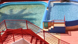 Una piscina amb un videt blau i vermell, una paret de pedra i una escala vermella que baixa cap a l'aigua.