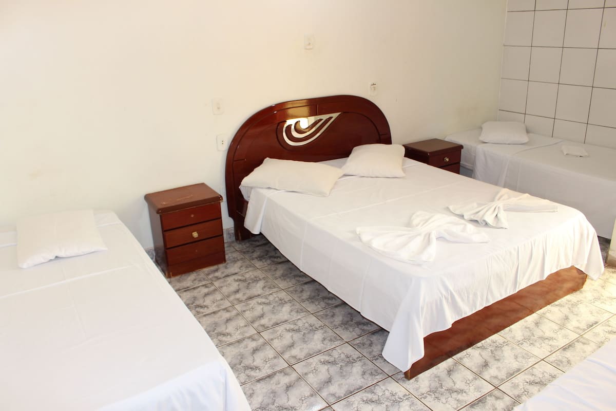 A hotel room with a large bed, two bedside tables, a wooden headboard, and a tiled floor.