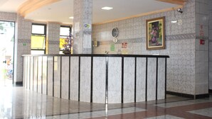 Zona de recepció amb un taulell de marbre, un rellotge i un quadre floral emmarcat a la paret.