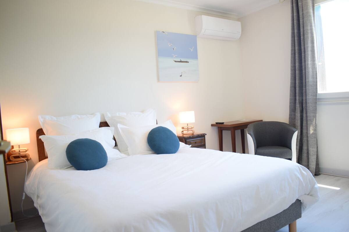 Quarto de hotel com uma cama grande, uma escrivaninha, uma cadeira e um quadro na parede.