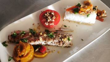 Un plato blanco con un trozo de pescado, un tomate y una porción de arroz blanco.