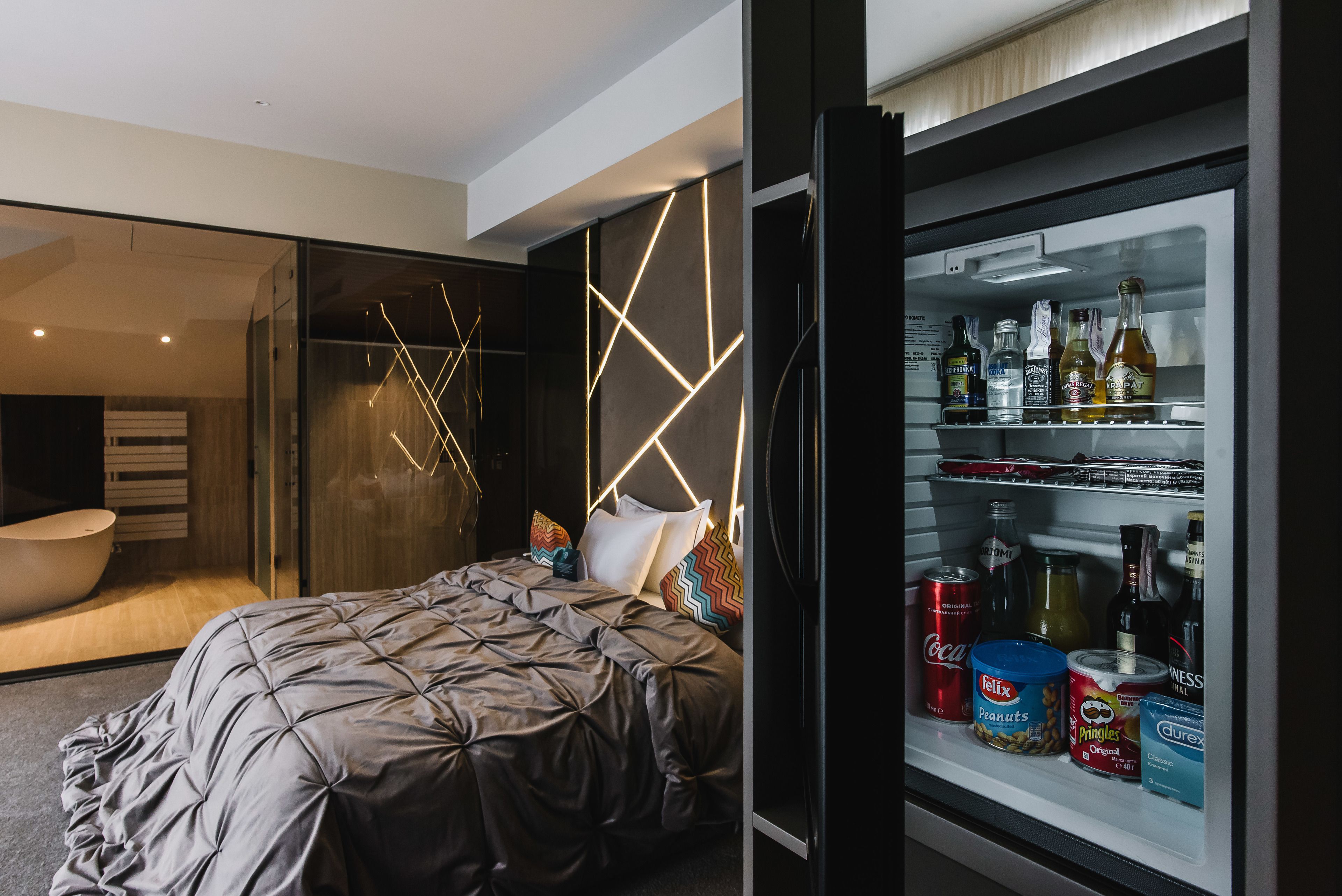 Un dormitorio moderno con cama, un minibar de vidrio y un baño con bañera.