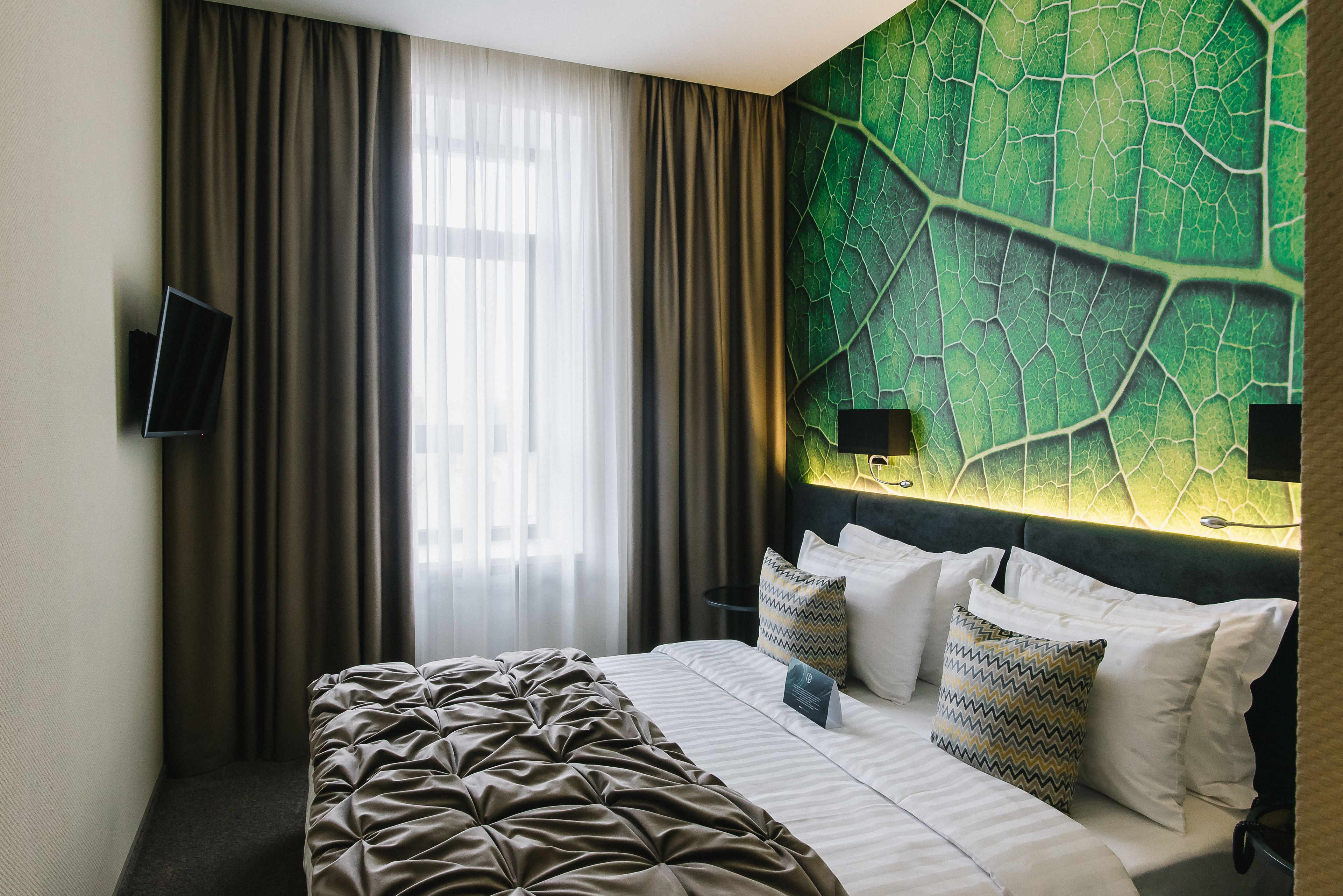 A hotel room with a large bed, a flat-screen TV mounted on the wall, and a green leaf-patterned wall.