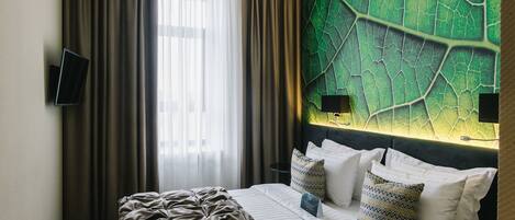 A hotel room with a large bed, a flat-screen TV mounted on the wall, and a green leaf-patterned wall.