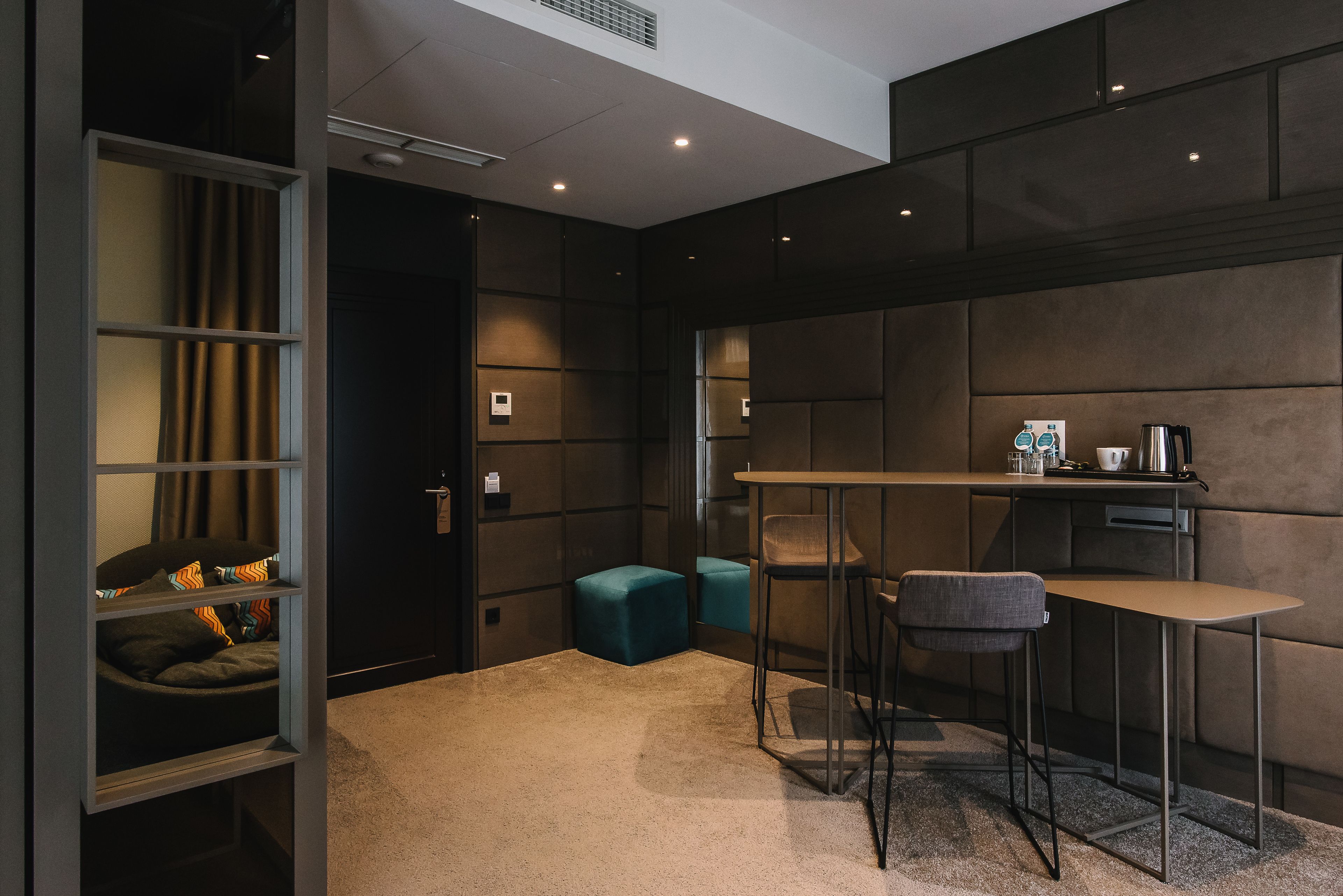 A modern, compact room with a kitchenette, a small seating area with a table and chairs, and a built-in shelving unit with a bed.