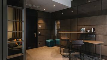 A modern, compact room with a kitchenette, a small seating area with a table and chairs, and a built-in shelving unit with a bed.