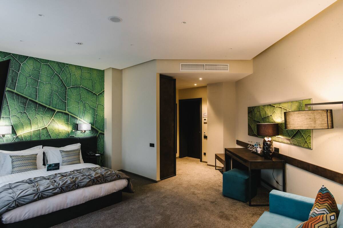 A modern hotel room with a large bed, a desk, and a seating area.