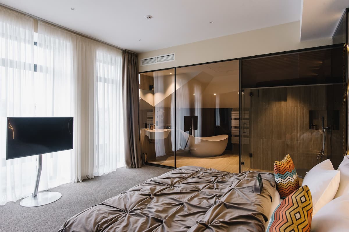 A modern hotel room with a large bed, a flat-screen TV, a glass-enclosed bathroom, and a sliding door closet.