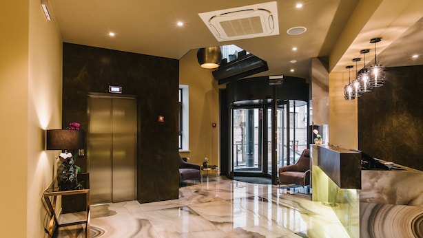 A lobby with a marble floor, a reception desk, a modern elevator, and a seating area with chairs. - Noble Boutique Hotel (Lutsk)