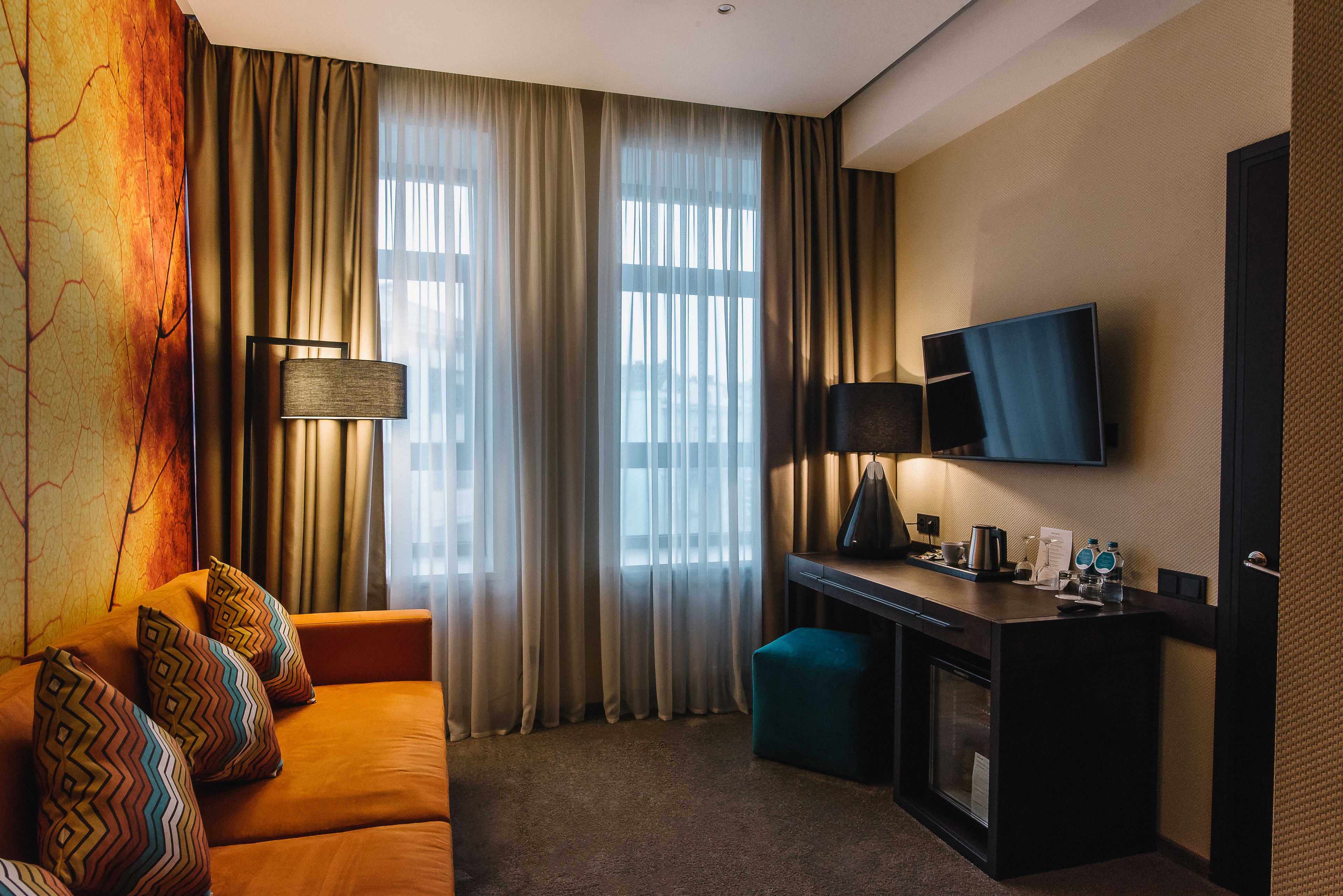 A hotel room with a sofa, a desk, a television, and a window with curtains.