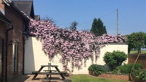 A brick building with a white wall and a garden area with a picnic table and potted plants. - Marsh Farm (Rugeley)