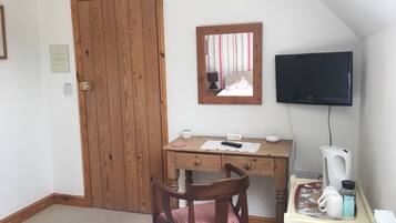 Ein Zimmer mit Holztür, Schreibtisch mit Spiegel, Fernseher und Stuhl.