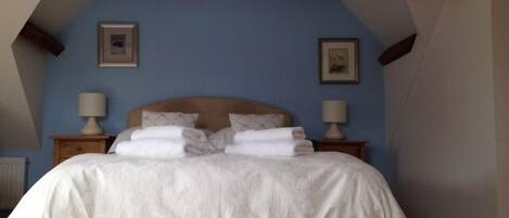 Un dormitorio con una cama, dos mesitas de noche con lámparas y dos cuadros en la pared.